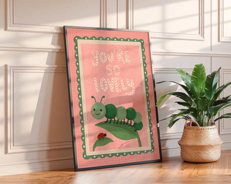 May include: A framed art print with the words "YOU'RE SO LOVELY" in white on a pink background. The print features a green caterpillar, a ladybug, and a green leaf. The frame is black.