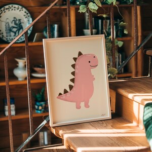 Pu&ograve; includere: Una stampa incorniciata con un'illustrazione di dinosauro rosa con dettagli marroni. Il dinosauro ha un'espressione amichevole ed &egrave; ambientato su uno sfondo color crema. L'opera d'arte &egrave; esposta su una scala di legno.