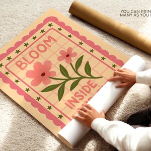 May include: A floral print poster with the words "BLOOM INSIDE" in pink. The poster has a pink scalloped border with green stars. A rolled-up poster and a brown tube are also visible.