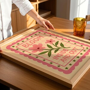 May include: A framed art print with the words "BLOOM INSIDE AND OUT" in a pink and green floral design. The print is in a light wood frame, and the overall aesthetic is cheerful and decorative.