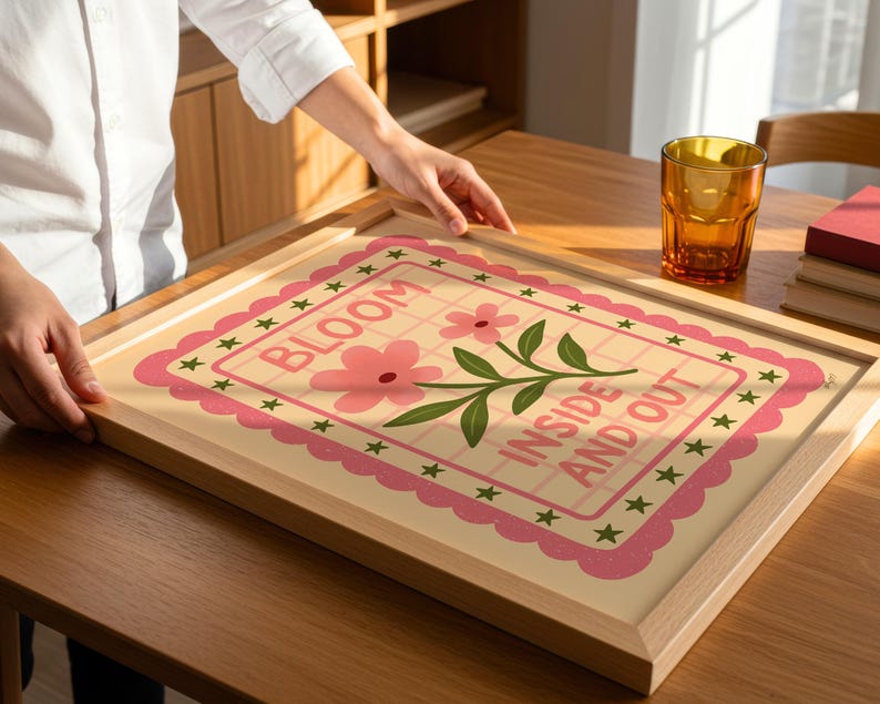 May include: A framed art print with the words "BLOOM INSIDE AND OUT" in a pink and green floral design. The print is in a light wood frame, and the overall aesthetic is cheerful and decorative.