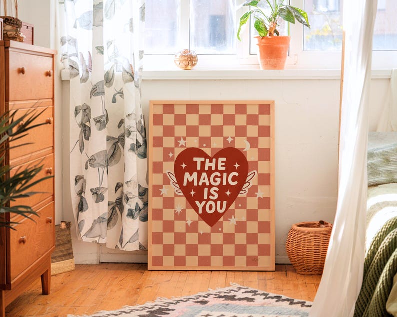 May include: A framed art print featuring a red and tan checkered pattern. The print has a red heart with white text that reads "THE MAGIC IS YOU". The heart has white wings and is surrounded by stars.