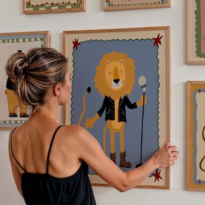 May include: A framed illustration of a lion wearing a black jacket and holding a microphone. The lion is set against a blue background with a scalloped border. Other framed illustrations of circus animals are visible.