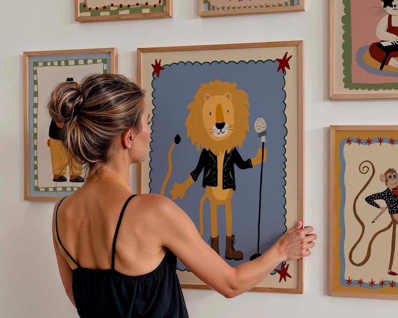 May include: A framed illustration of a lion wearing a black jacket and holding a microphone. The lion is set against a blue background with a scalloped border. Other framed illustrations of circus animals are visible.