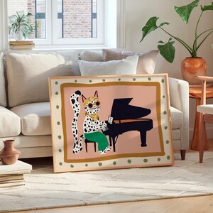 May include: A framed illustration of a spotted cat playing a piano. The cat is wearing green pants and has a pink background. The frame is wood with a gold border.