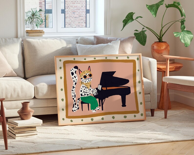 May include: A framed illustration of a spotted cat playing a piano. The cat is wearing green pants and has a pink background. The frame is wood with a gold border.