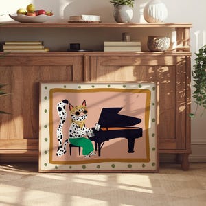 May include: A framed illustration of a spotted cat wearing sunglasses and a bandana playing a black grand piano. The background is a light pink with a gold and green border.
