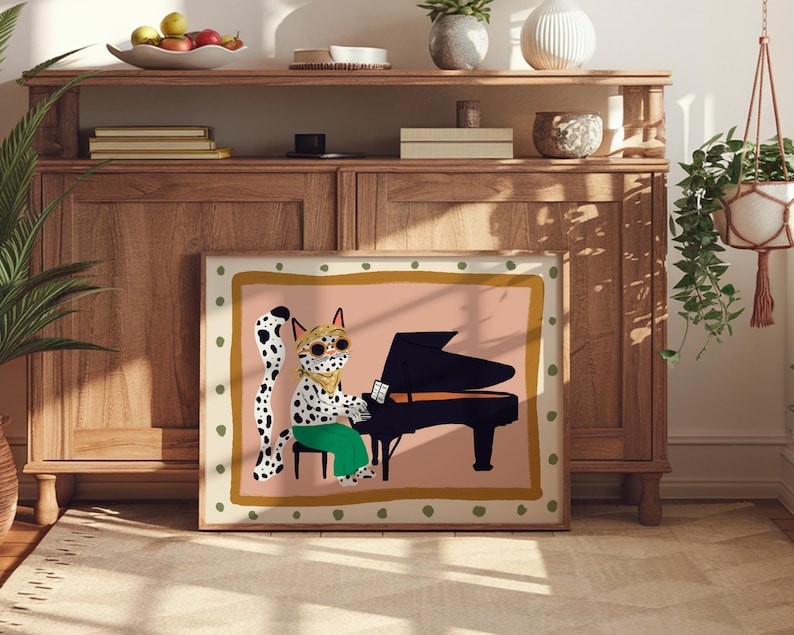 May include: A framed illustration of a spotted cat wearing sunglasses and a bandana playing a black grand piano. The background is a light pink with a gold and green border.
