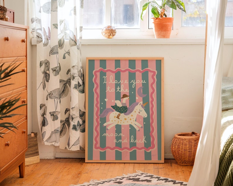 May include: A framed print with a pink and teal striped background features a whimsical illustration of a unicorn with a rider. The text "I love you to the moon and back" is displayed in a decorative font. The artwork is set in a room with natural light.