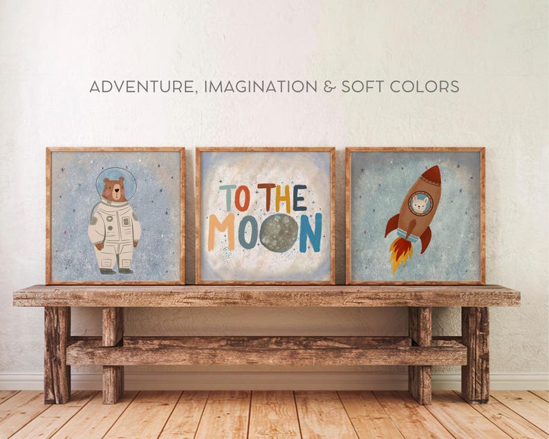 May include: Three framed illustrations with a space theme. The first shows a brown bear wearing an astronaut suit. The second shows a moon with the text "To the Moon". The third shows a rocket with a white cat inside. The illustrations are on a wooden shelf.