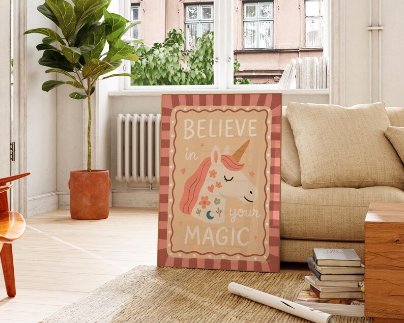 May include: A framed canvas print featuring a whimsical unicorn illustration with the text "BELIEVE in your MAGIC." The artwork has a tan background with a pink and red plaid border. The unicorn has a golden horn and pink mane.