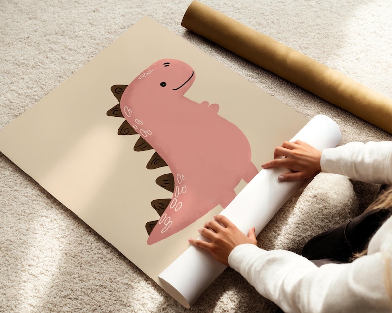 Pu&ograve; includere: Illustrazione di un dinosauro rosa su un poster beige. Il dinosauro ha un'espressione amichevole e spine marroni sulla schiena. Sono visibili anche un poster arrotolato e un tubo marrone.