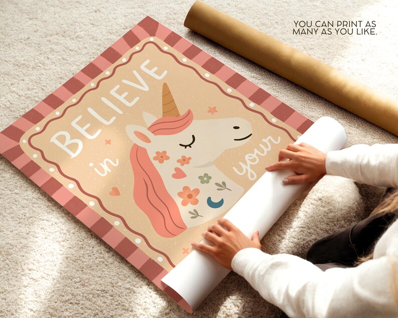 May include: A rolled-up poster featuring a unicorn illustration with the words "BELIEVE in your" in white. The unicorn has a pink mane and floral accents. The poster is on a light-colored surface.