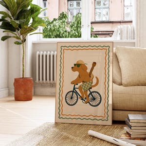 May include: A framed art print featuring a cartoon dog riding a bicycle. The dog wears sunglasses, a hat, and shorts, with a guitar strapped to its back. The artwork has a cream background with a decorative border in green and orange.