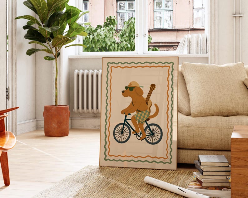 May include: A framed art print featuring a cartoon dog riding a bicycle. The dog wears sunglasses, a hat, and shorts, with a guitar strapped to its back. The artwork has a cream background with a decorative border in green and orange.