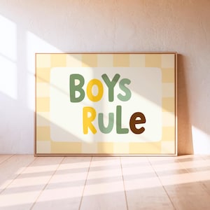 Puede incluir: Un cuadro enmarcado con la frase "BOYS RULE" en letras coloridas. El fondo es un patrón de cuadros amarillos claros con un rectángulo blanco en el centro. El marco es de color marrón claro.