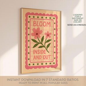 May include: A framed art print with a floral design. The artwork features the word "BLOOM" above two pink flowers and the phrase "INSIDE AND OUT". The print has a pink scalloped border with stars and is in a gold frame.