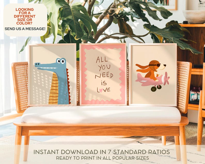 Op de afbeelding: Drie ingelijste kunstafdrukken met cartoonillustraties. E&eacute;n toont een blauwe alligator, een andere heeft de tekst "ALL YOU NEED IS LOVE", en de derde toont een hond in een vliegtuig. De prints worden op een houten bank getoond.