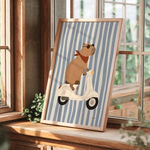 framed capybara scooter poster leaning against molded wall with tropical plant coastal kids room decor blue stripe nursery art