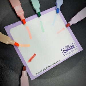 May include: A purple notecard with the text "TODAY I CHOOSE joy" and "UNWAVERING GRACE" written on it. The notecard is surrounded by colorful highlighters.
