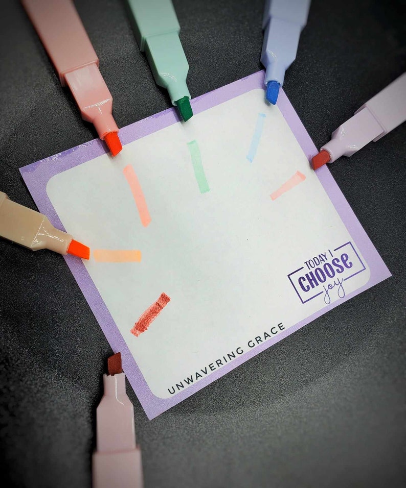 May include: A purple notecard with the text "TODAY I CHOOSE joy" and "UNWAVERING GRACE" written on it. The notecard is surrounded by colorful highlighters.