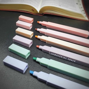 May include: Set of pastel highlighters with matching caps. The highlighters have a square barrel and a chisel tip. The colors are pink, lavender, light yellow, light green, and light blue. The text "UNWAVERING GRACE" is printed on one of the highlighters.