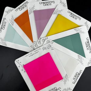 May include: A set of 7 colorful sticky note pads with the text "Unwavering Grace" and "Lathyrus Bloom 50 sheets 3x3 inches" printed on the front. The colors of the sticky notes are pink, yellow, green, orange, purple, light blue, and white.