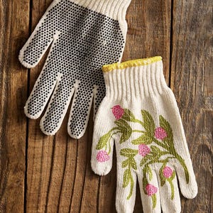May include: A pair of off-white gardening gloves. One glove has a black dotted palm, the other features a floral design with pink flowers and green leaves. Both gloves have yellow trim.