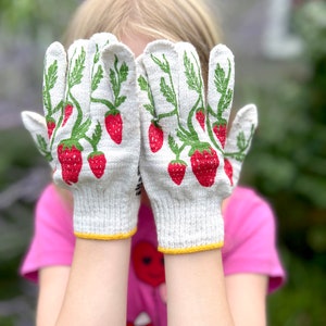 Puede incluir: Un par de guantes de jardiner&iacute;a de algod&oacute;n blanco con estampado de fresas. Los guantes tienen un ribete amarillo alrededor de las mu&ntilde;ecas.