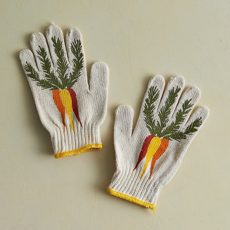 K&ouml;nnte beinhalten: Ein Paar wei&szlig;e Baumwoll-Gartenhandschuhe mit einem gr&uuml;nen und orangefarbenen Karotten-Design.