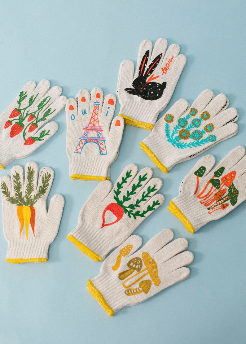 May include: Set of 8 white cotton gardening gloves with colorful hand-painted designs. The designs include strawberries, a carrot, a radish, mushrooms, a bunny, flowers, and the Eiffel Tower with the word "oui".
