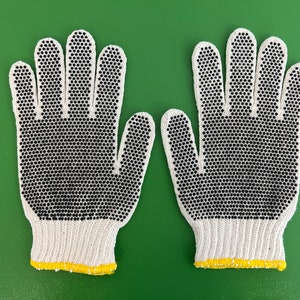 May include: A pair of white cotton work gloves with black rubberized dots on the fingertips and palms. The gloves have a yellow trim around the wrist.