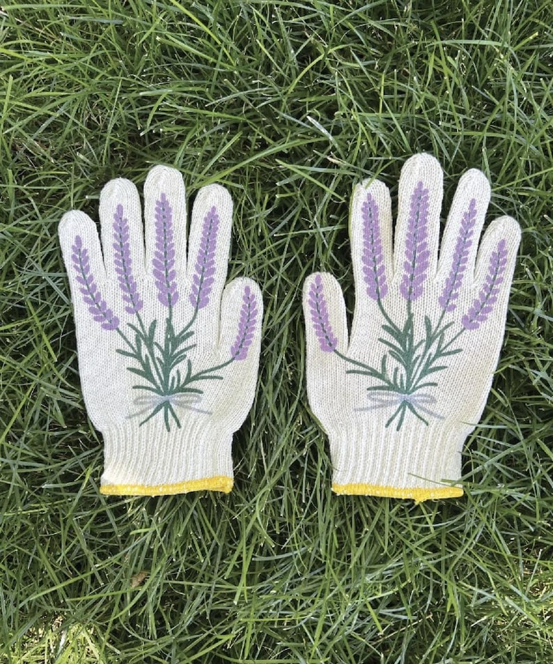 May include: A pair of gardening gloves with a lavender design. The gloves are off-white with a yellow trim at the wrist. Lavender sprigs are printed on the back of each glove in purple and green.