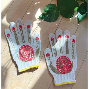 May include: A pair of white gardening gloves with a yellow trim. The gloves feature a red and brown snail design with mushrooms on the fingers.