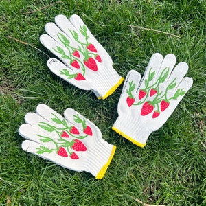May include: Two pairs of white gardening gloves with yellow trim. The gloves have a green and red strawberry design.