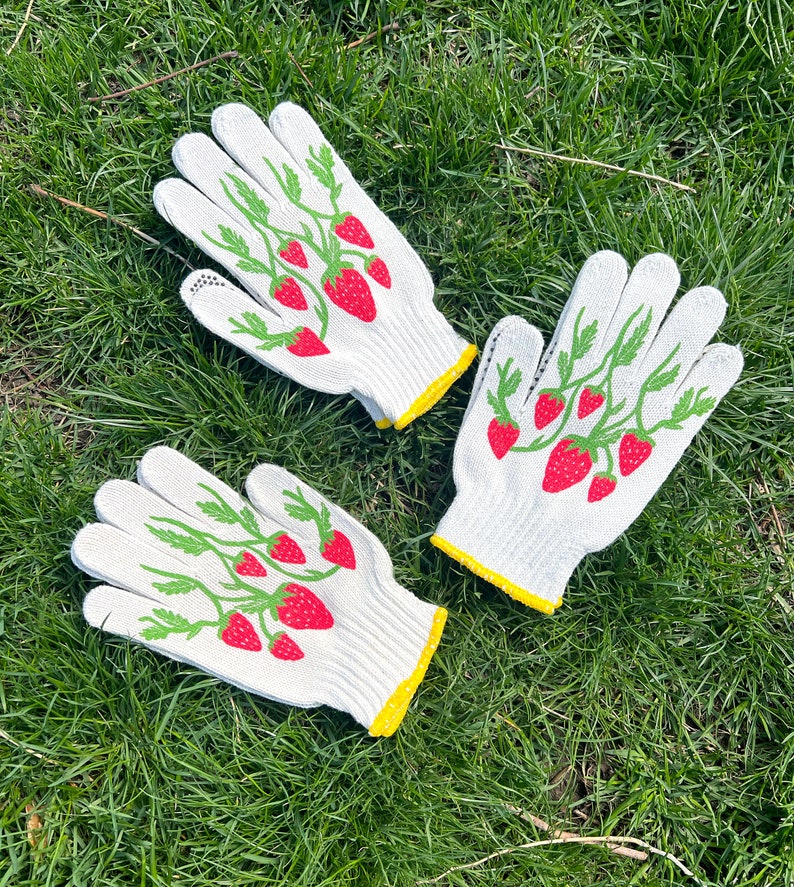 May include: Two pairs of white gardening gloves with yellow trim. The gloves have a green and red strawberry design.