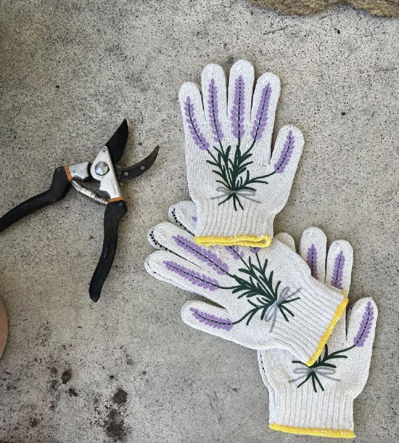 May include: White gardening gloves with lavender sprig embroidery and yellow trim are paired with black and silver pruning shears. The gloves feature purple lavender and green leaves, perfect for gardening.