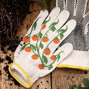 May include: White gardening gloves with a tomato plant design. The gloves have a yellow trim and a dotted pattern on the palm. The design features orange tomatoes and green leaves.