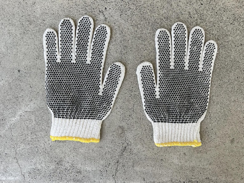 May include: Pair of white work gloves with black dotted grips. The gloves have a ribbed cuff with a yellow trim. The gloves are designed for protection and grip, suitable for various tasks.