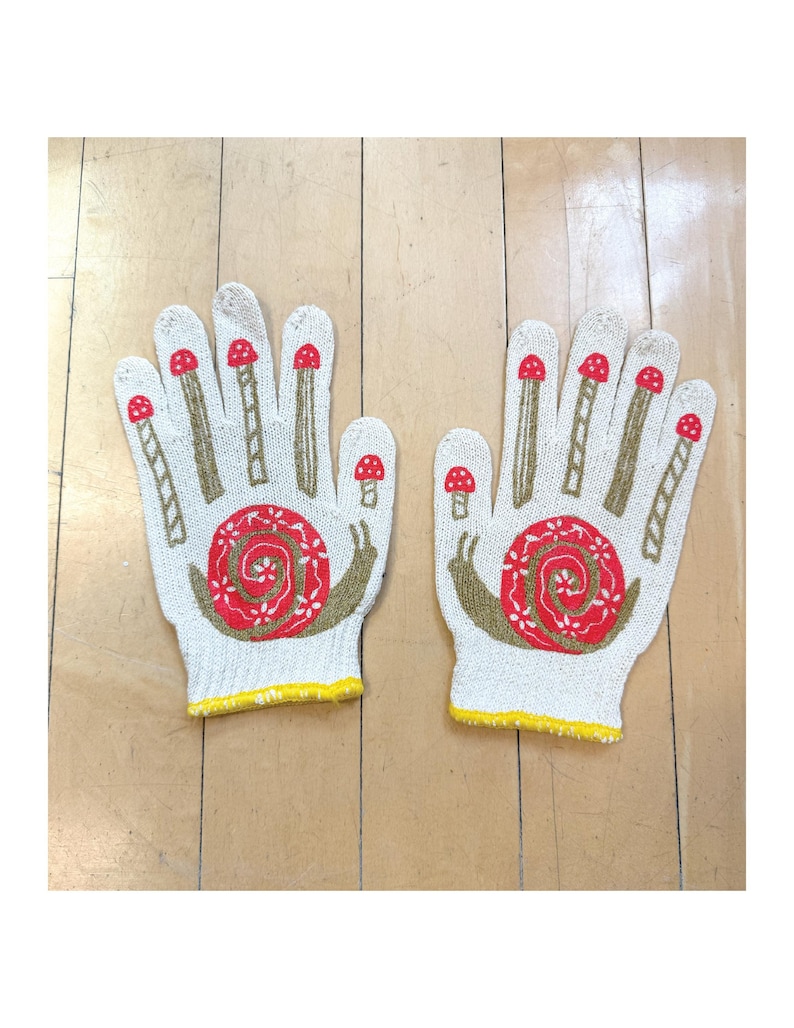 May include: A pair of white cotton work gloves with a yellow trim. The gloves have a red and green snail design with mushrooms on the fingers.
