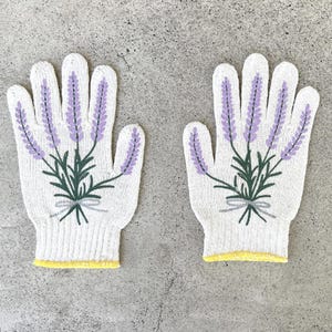 May include: A pair of white knitted gloves with a lavender floral design. The gloves feature purple lavender sprigs with green leaves and stems, tied with a gray bow. The cuffs have a yellow trim.