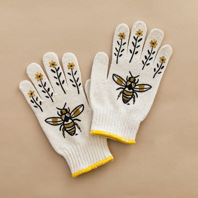 Puede incluir: Un par de guantes de jardiner&iacute;a de algod&oacute;n blanco con ribete amarillo. Los guantes tienen un dise&ntilde;o bordado de abeja y flores.