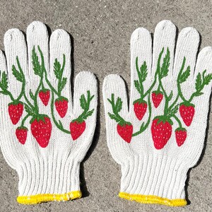 Puede incluir: Un par de guantes de jardiner&iacute;a de algod&oacute;n blanco con ribete amarillo y dise&ntilde;o de fresas. Los guantes tienen un patr&oacute;n de fresas rojas y verdes en la parte posterior de la mano.