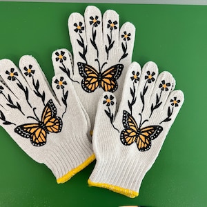 May include: Three white gardening gloves with yellow trim. Each glove has a black butterfly and white daisy designs.