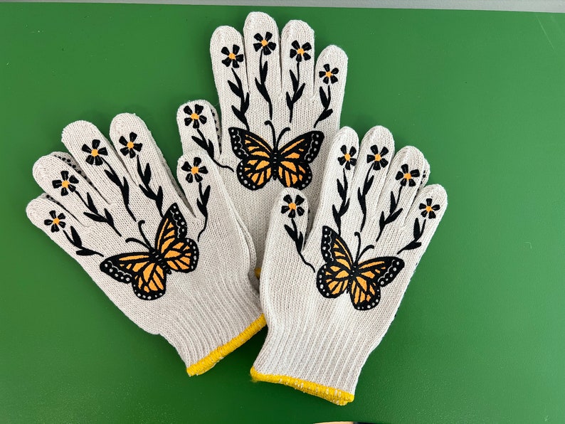 May include: Three white gardening gloves with yellow trim. Each glove has a black butterfly and white daisy designs.