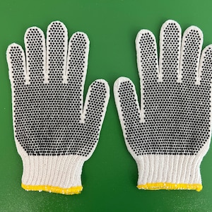 May include: A pair of white cotton work gloves with black rubberized dots on the fingertips and palms. The gloves have a yellow trim around the wrists.