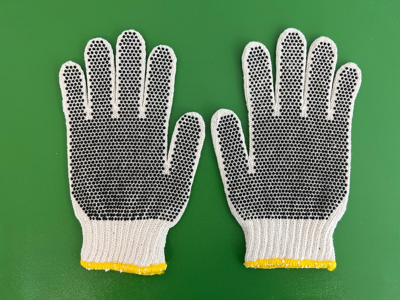 May include: A pair of white cotton work gloves with black rubberized dots on the fingertips and palms. The gloves have a yellow trim around the wrists.