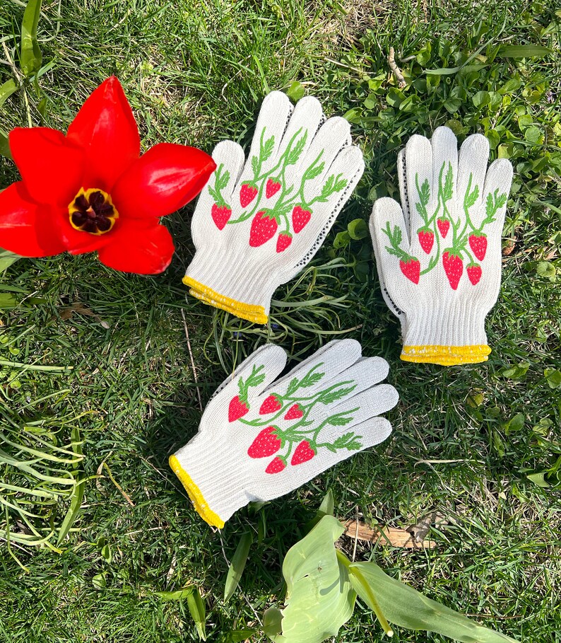 May include: Three pairs of white gardening gloves with a strawberry design. The gloves have yellow trim around the wrist.