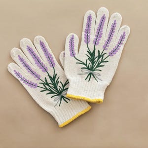 May include: A pair of off-white gardening gloves with a lavender floral design. The gloves feature purple lavender sprigs with green leaves and a gray bow. The cuffs are trimmed with yellow.