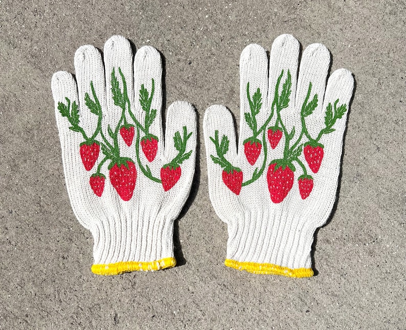 May include: A pair of white gardening gloves with a red and green strawberry design.